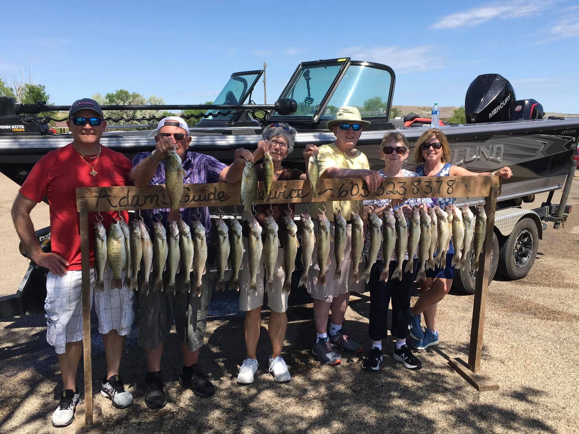 Group of people pose with a wooden fish rack filled with fish, a boat in the background.