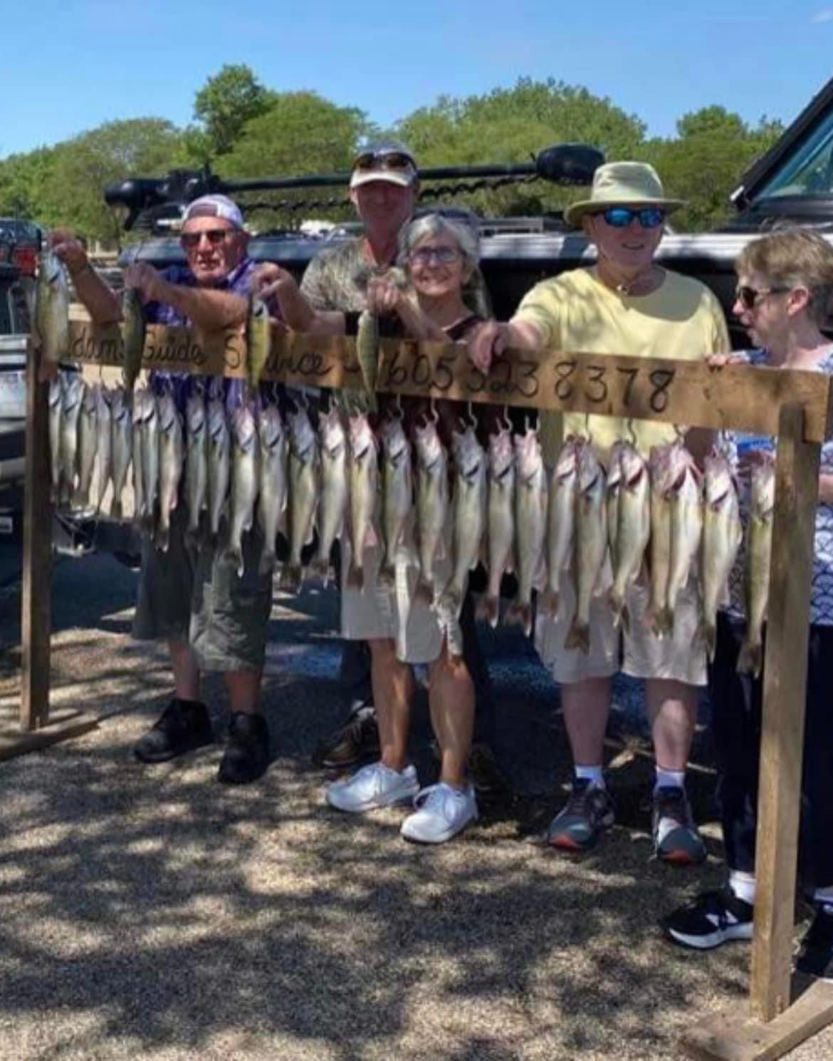 Five people stand with a wooden rack of caught fish. Blue sky.