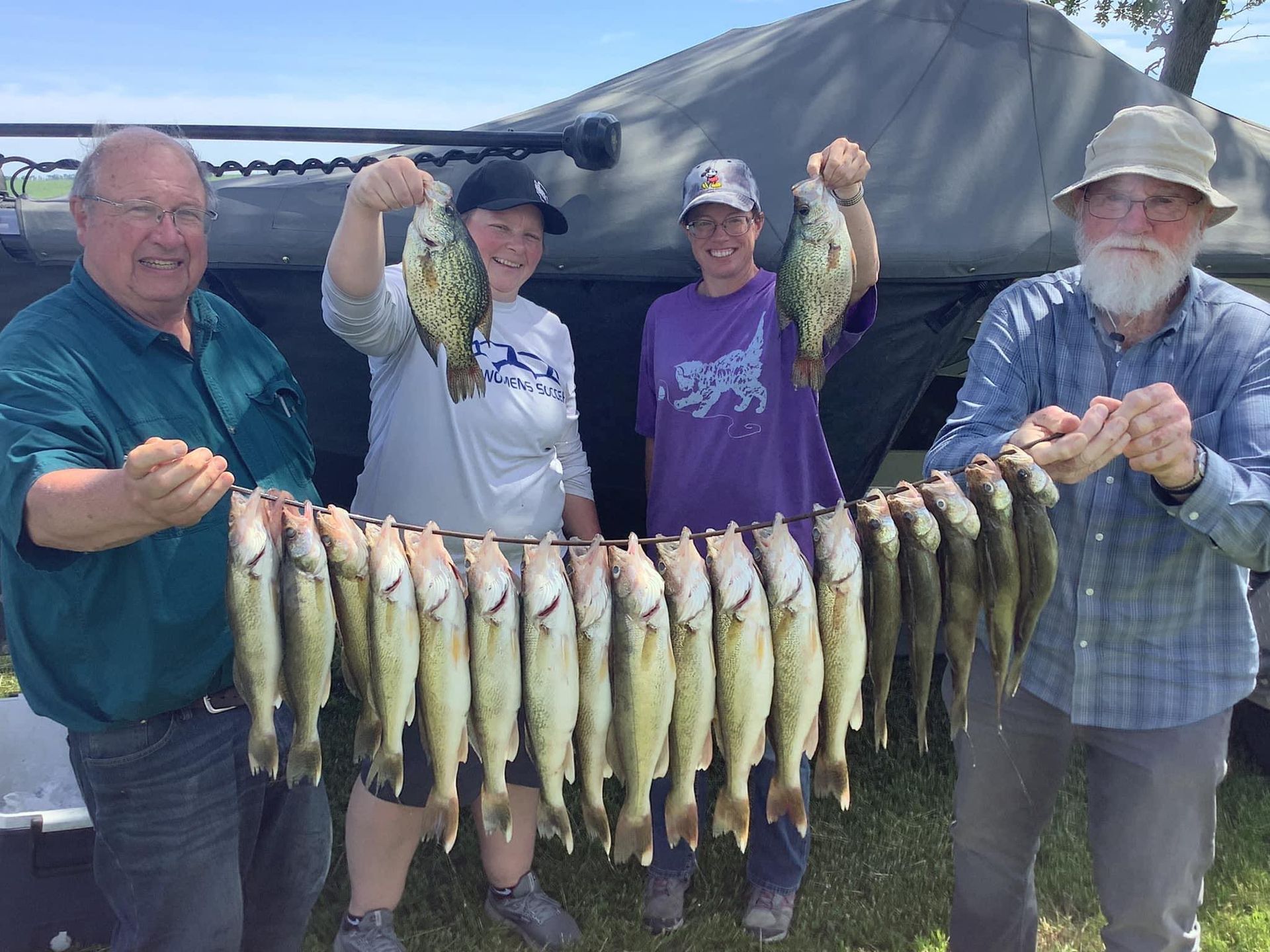 Four people proudly display a large catch of fish, likely after fishing trip.