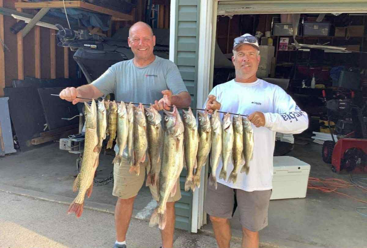 Two men holding a string of caught South Dakota Lake Thompson walleye, outside a garage.
