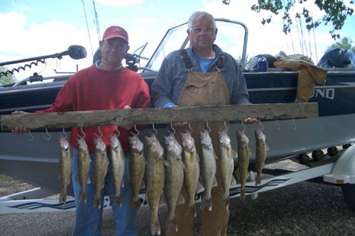 Two men holding a wooden stringer with a row of caught fish in front of a boat.