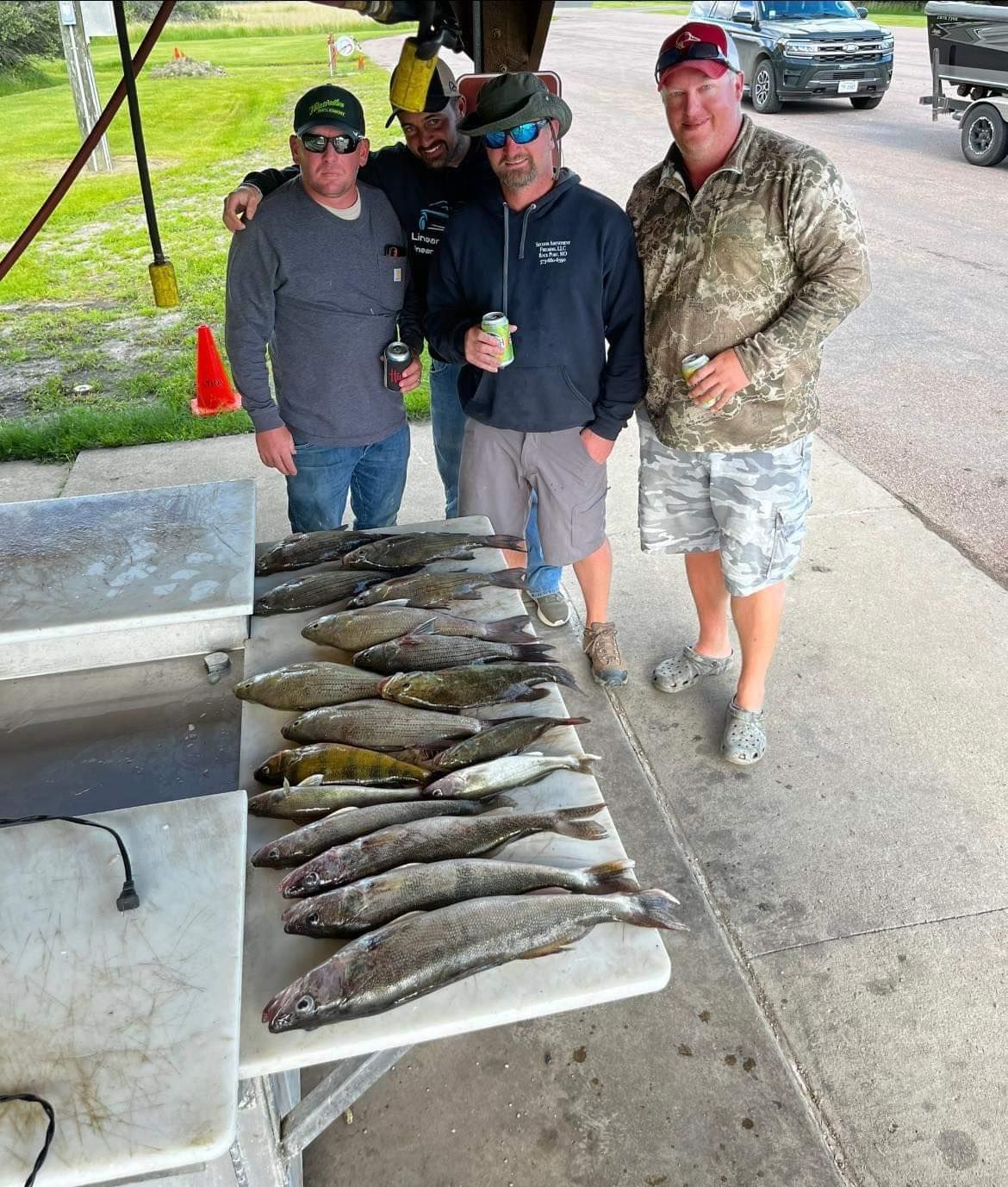 Four men pose with a table displaying a large catch of fish, outdoors.