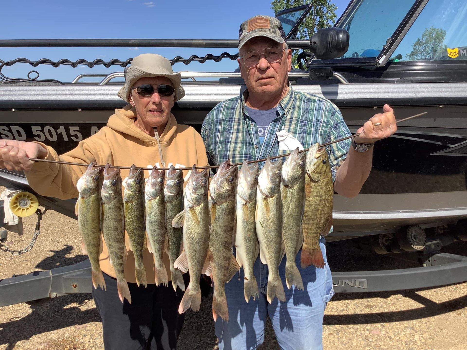 Two people holding up a string of caught fish near a boat.