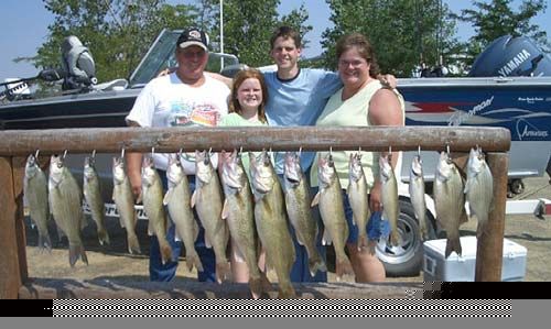Family posing with large catch of fish, near boats on a sunny day.