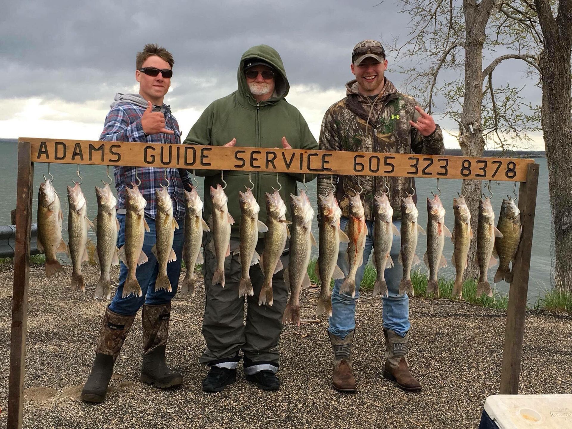 Three people with a string of caught fish under the sign 