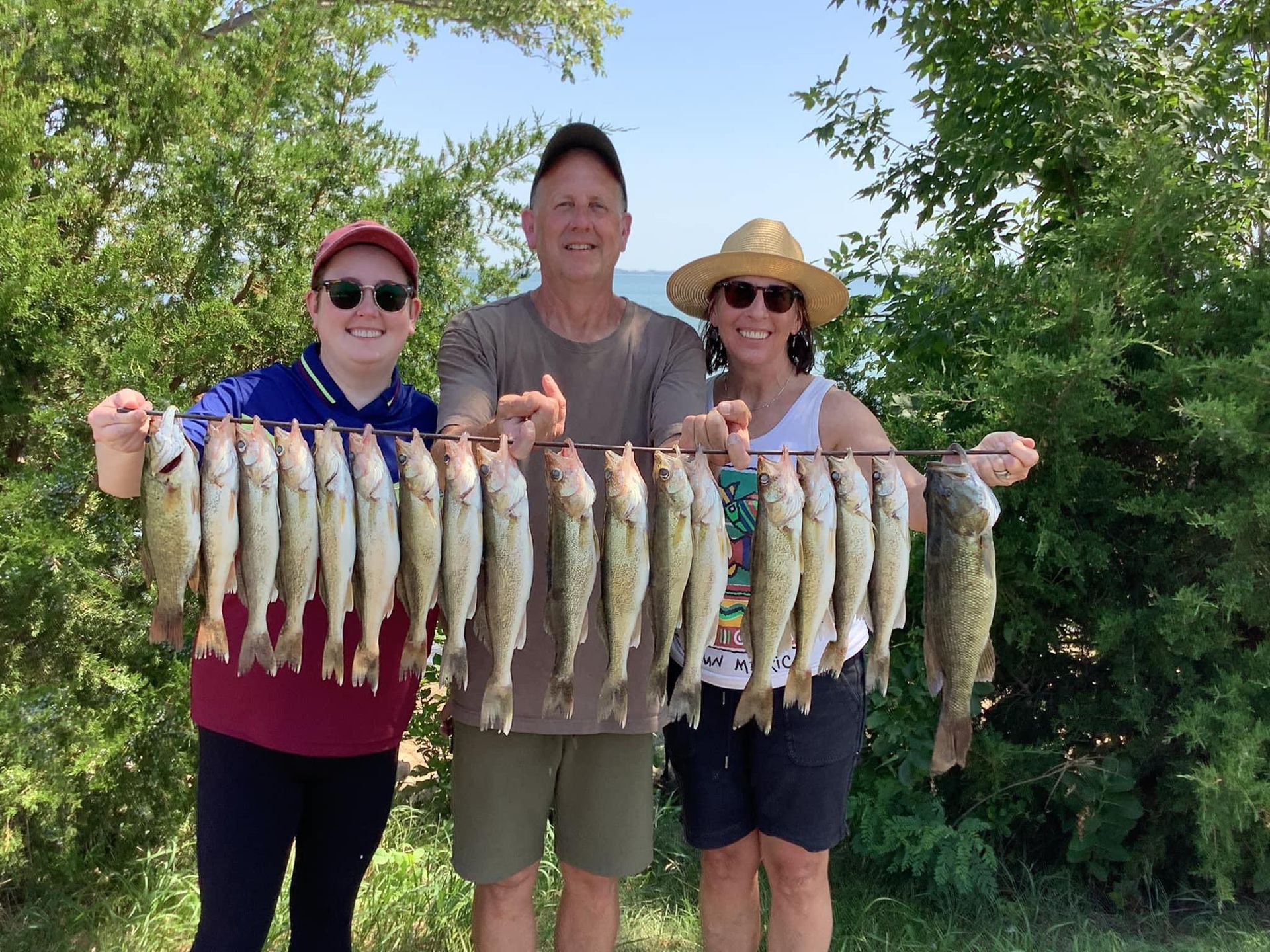 Three people hold up a string of caught fish, smiling, against a green background.