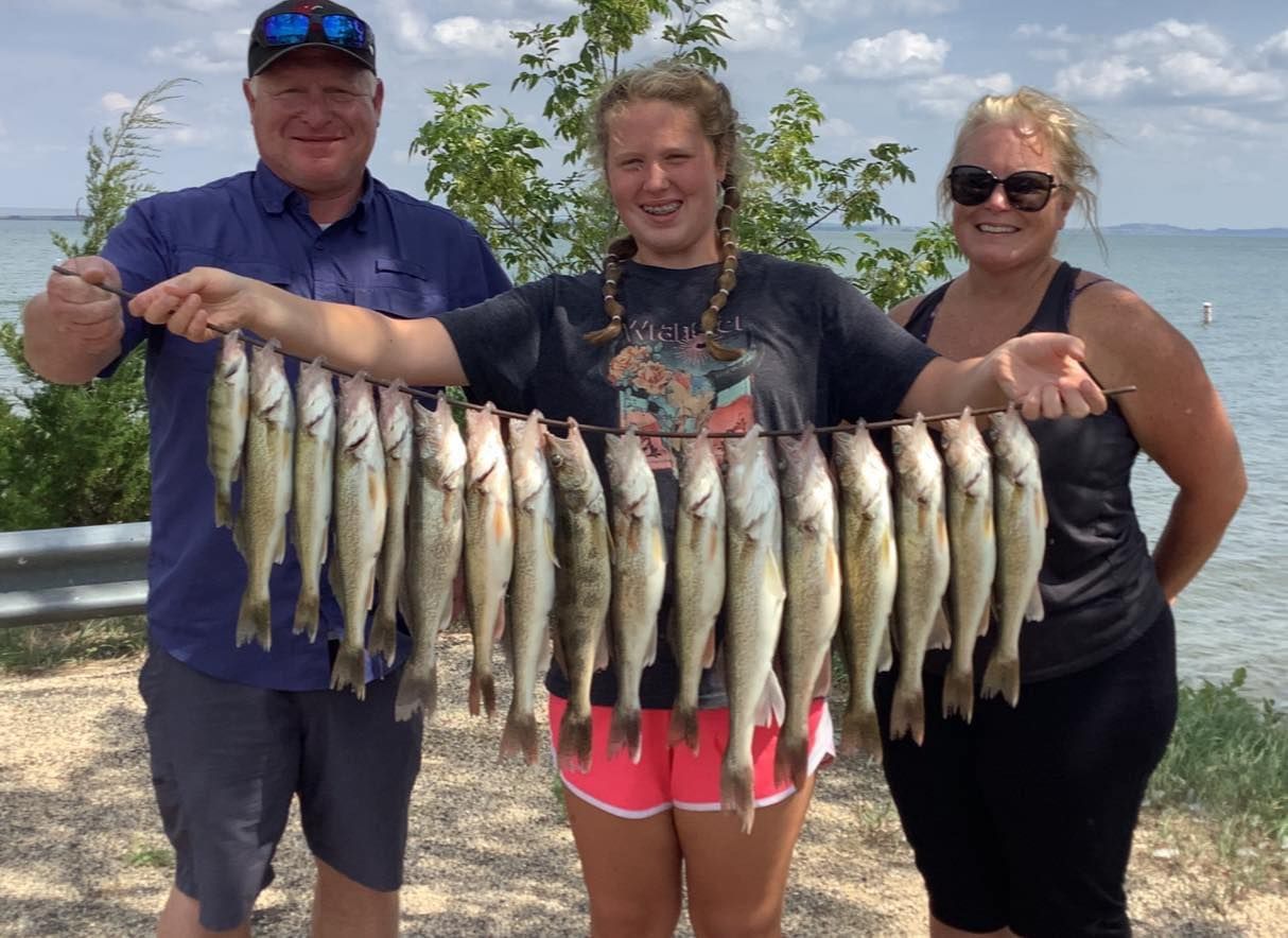 Three people holding up a string of caught fish near a body of water.