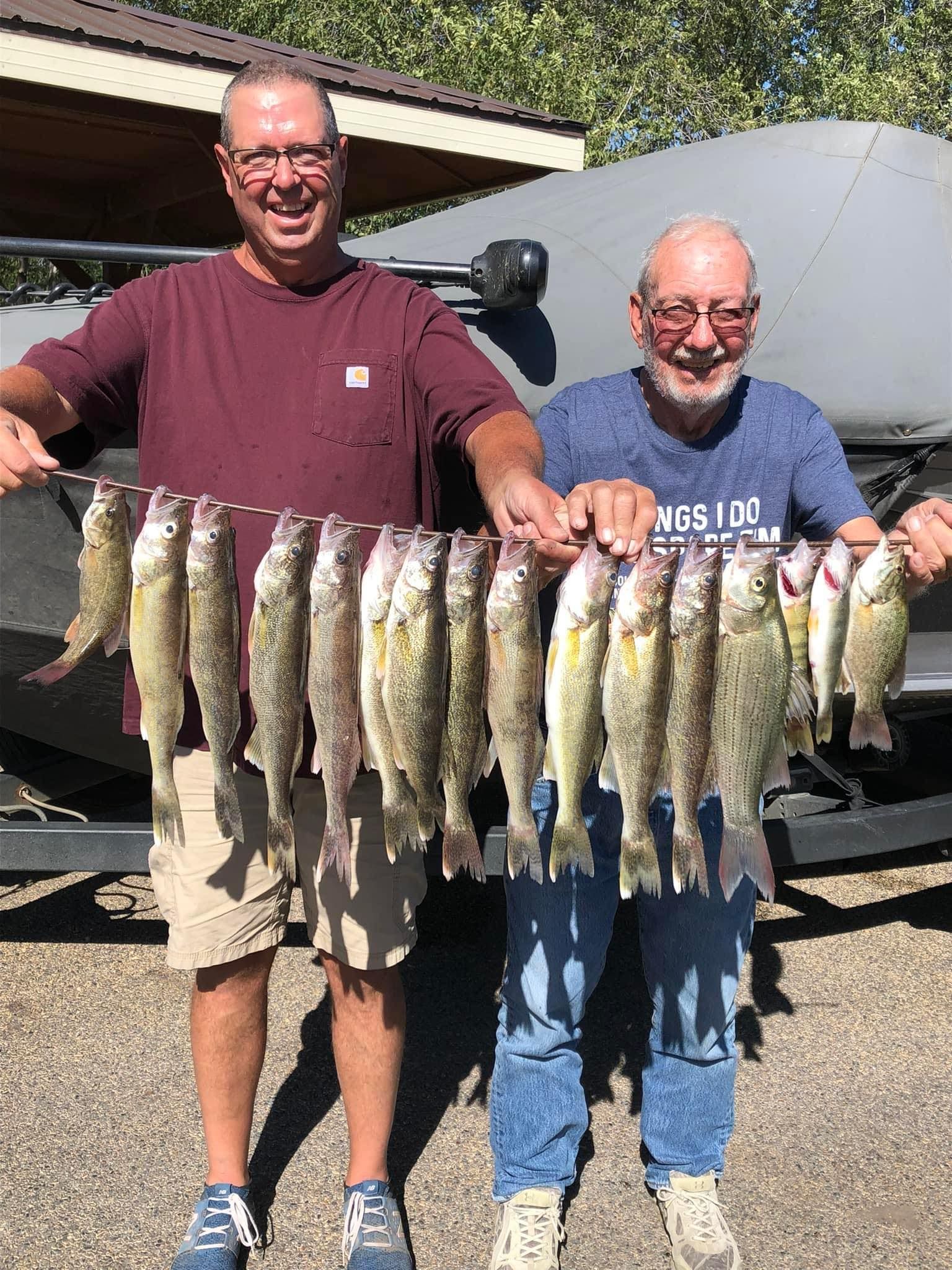 Two men holding up a string of caught fish in front of a boat, smiling.