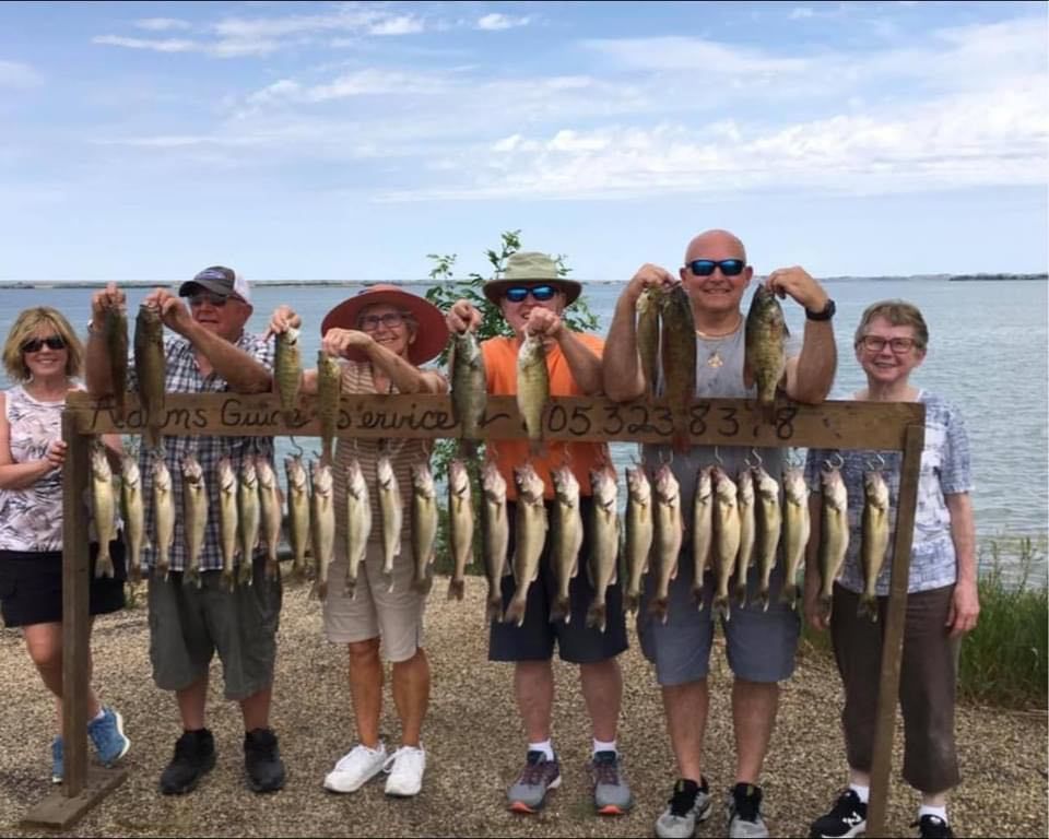 Group of people holding up a wooden rack with many fish caught, near a lake.