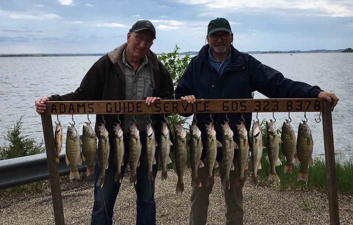 Two men holding a frame of caught fish, near water with a cloudy sky. 