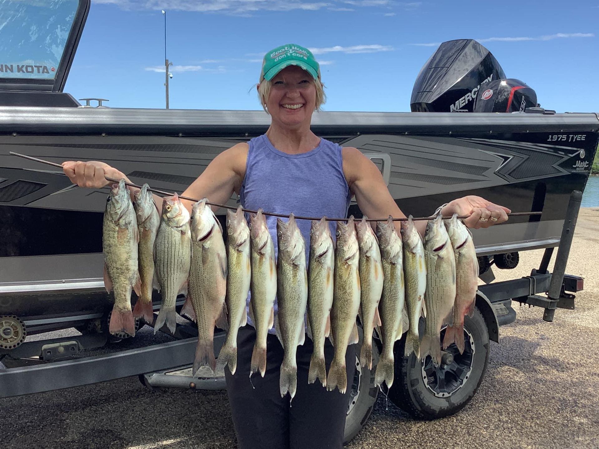 Woman holding a string of fish caught from a boat, in front of a blue sky and water.