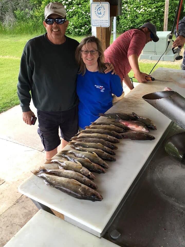 Man and woman pose with a row of fish on a cleaning table; another person cleans fish in background.