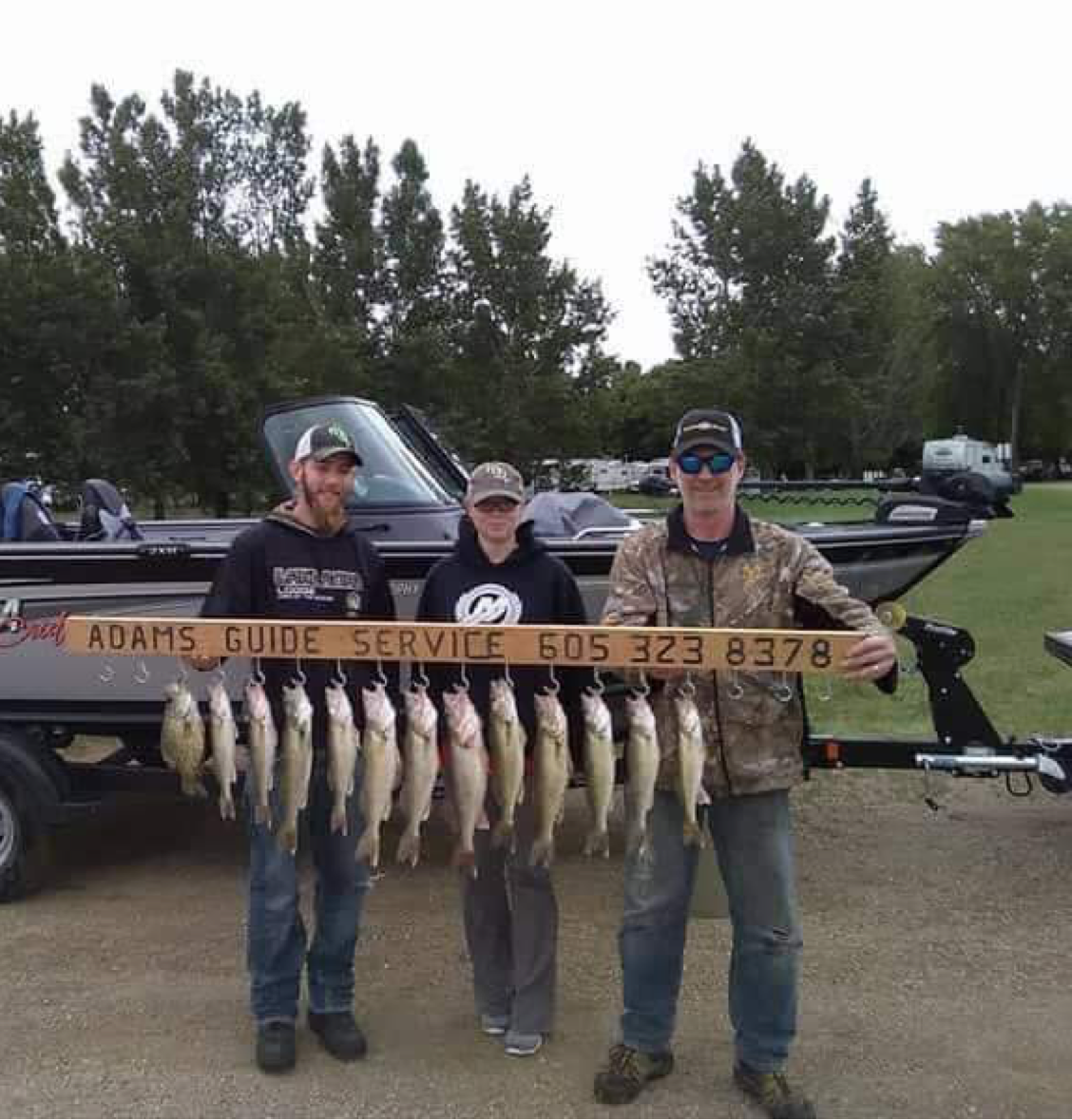 Three people holding a string of caught fish in front of a boat, advertising fishing guide service.