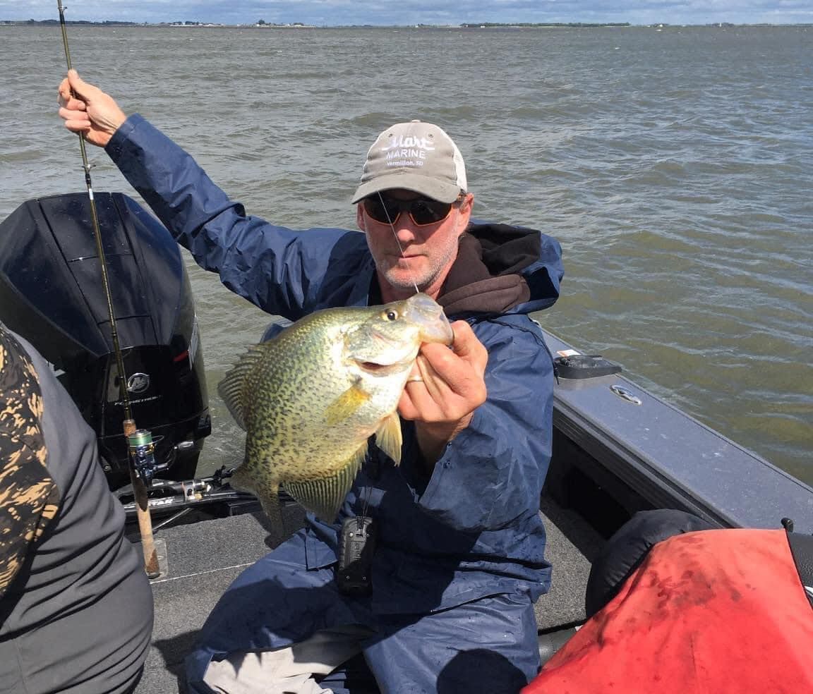 Man on boat holding up a freshly caught crappie.