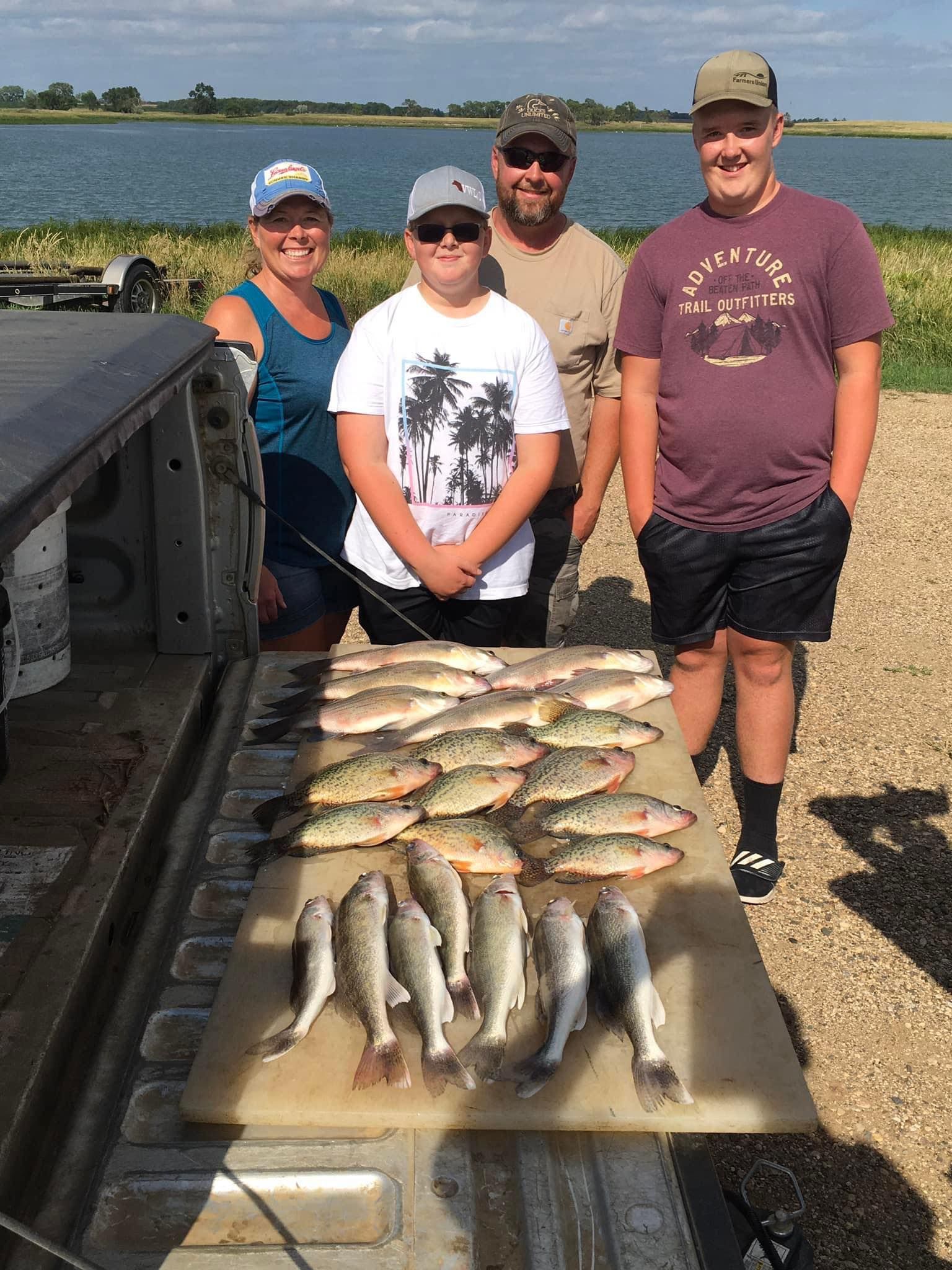Family stands by truck bed displaying many fish caught at a lake.