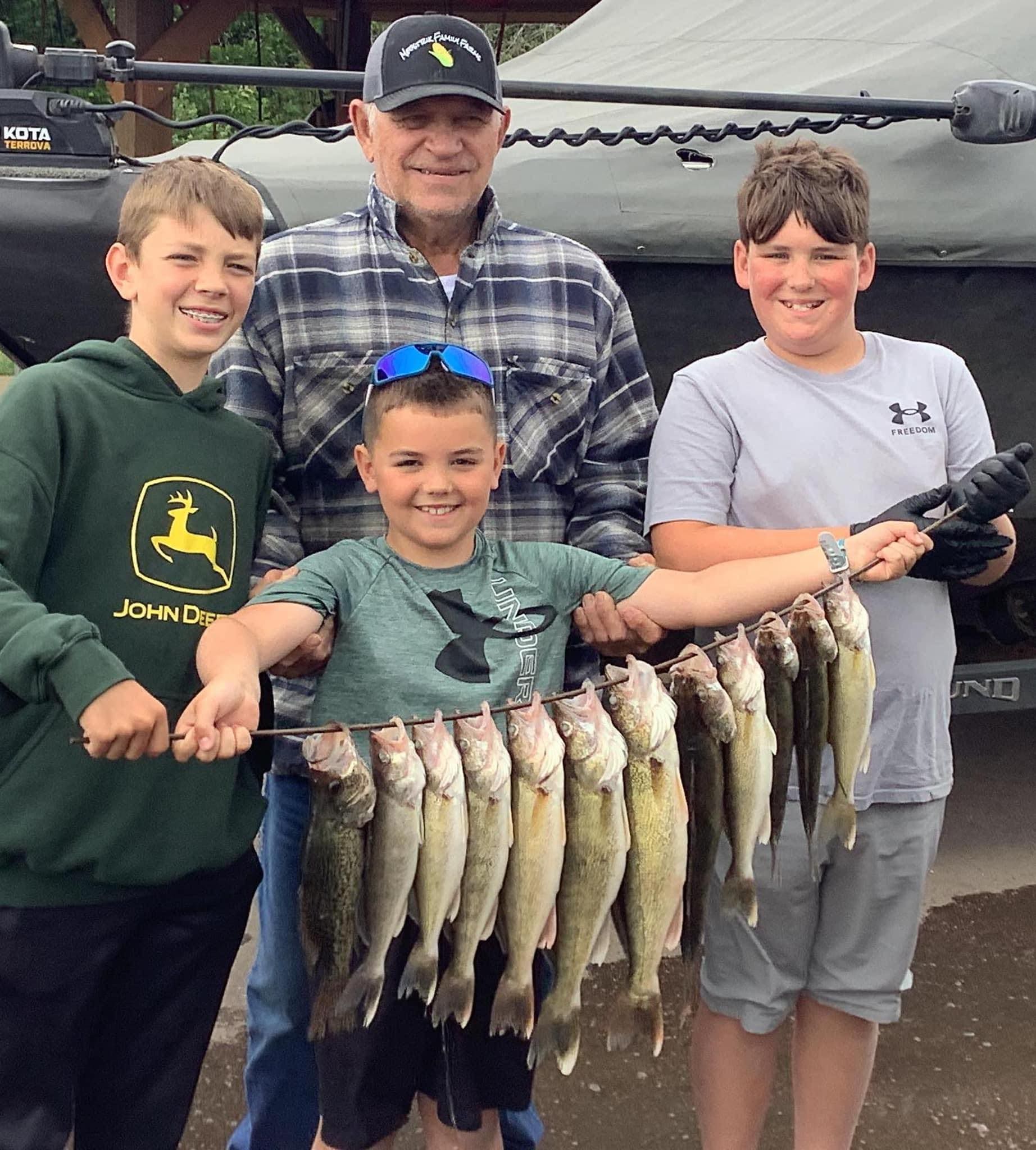 Group of people holding a string of fish, smiling. Outdoors near a boat.
