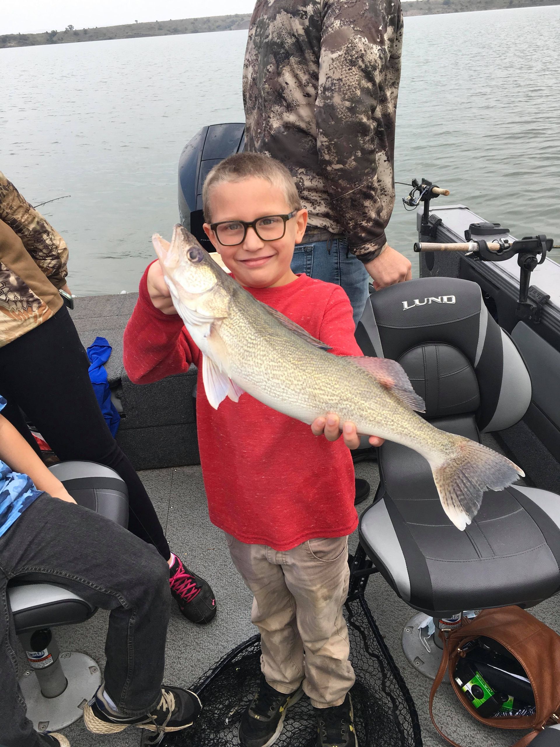 Boy in red shirt, holding a fish, smiles on a boat.
