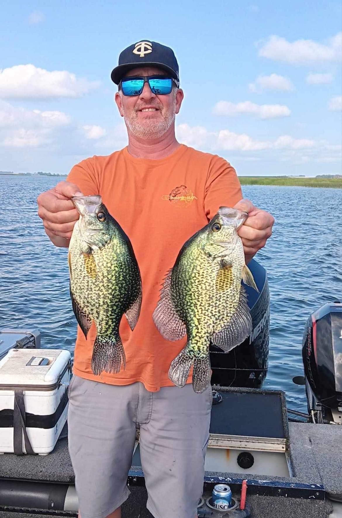 Man on boat holding up two crappie fish.