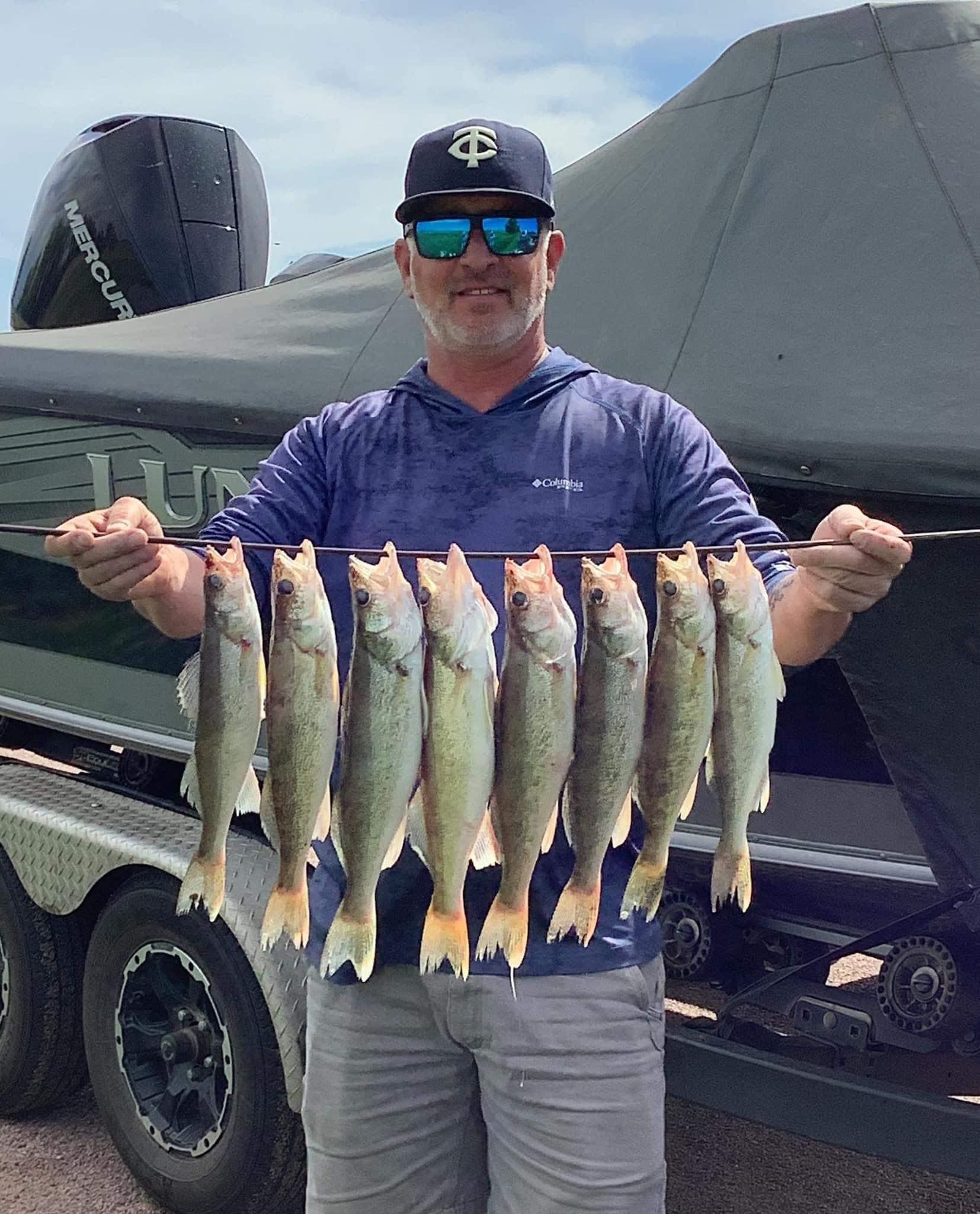 Man holding a string of nine walleye fish he caught near his Lund Tyee. He is wearing sunglasses and a hat.