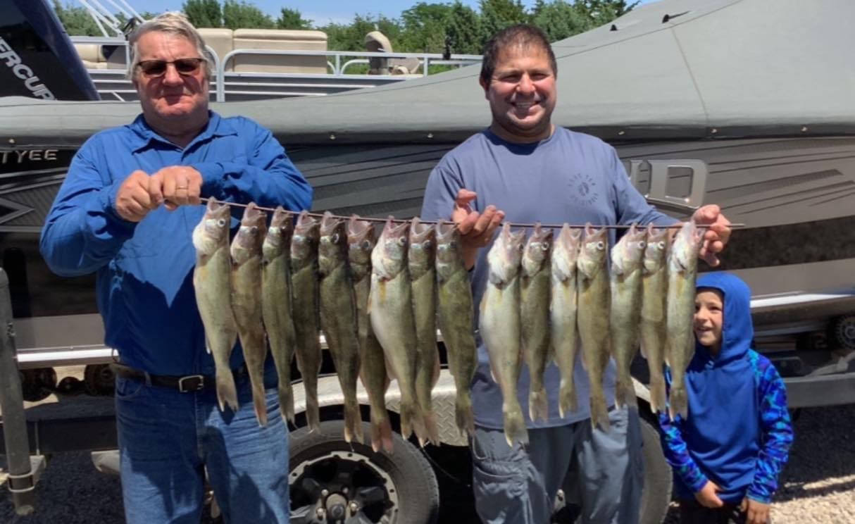 Two men and a child display a string of caught fish near a boat.