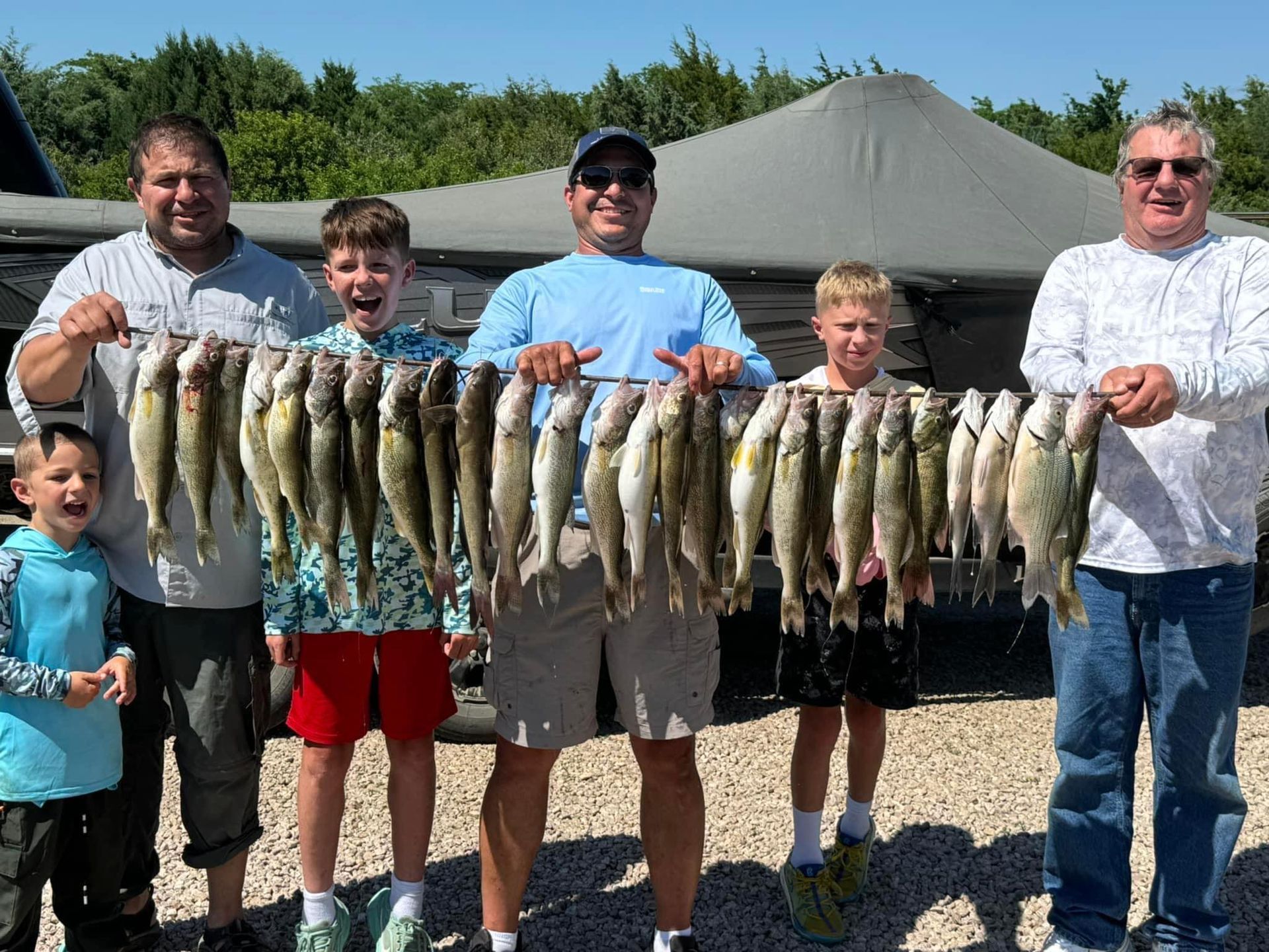 Five people holding up a string of caught fish on a sunny day.