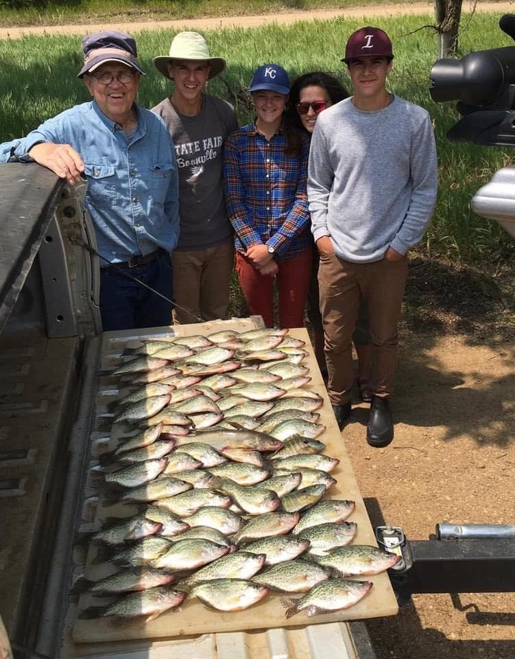 Group of people standing with a large catch of fish on a truck bed in a sunny outdoor setting.