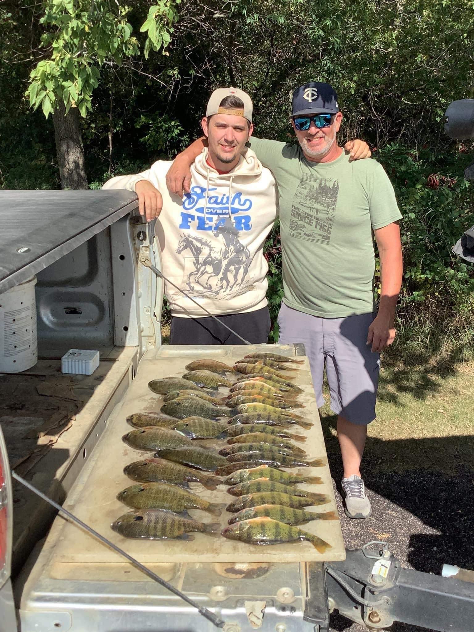 Two men stand with a truck bed filled with caught fish.