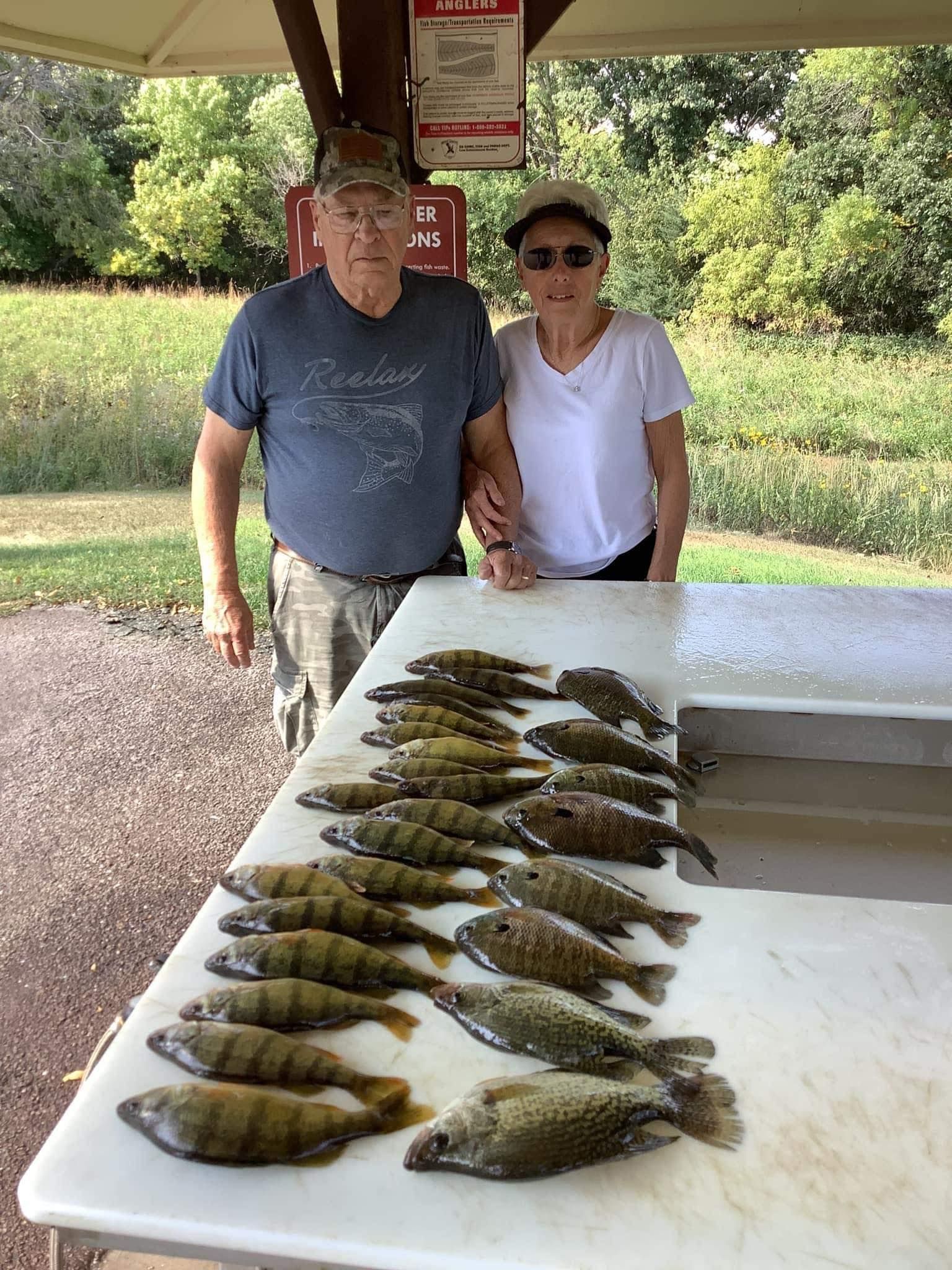 A couple stands by a table with many fish, likely a catch at a park.