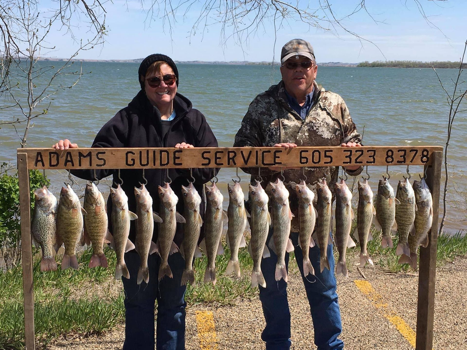 Two people holding a rack of caught fish with a sign for Adams Guide Service.