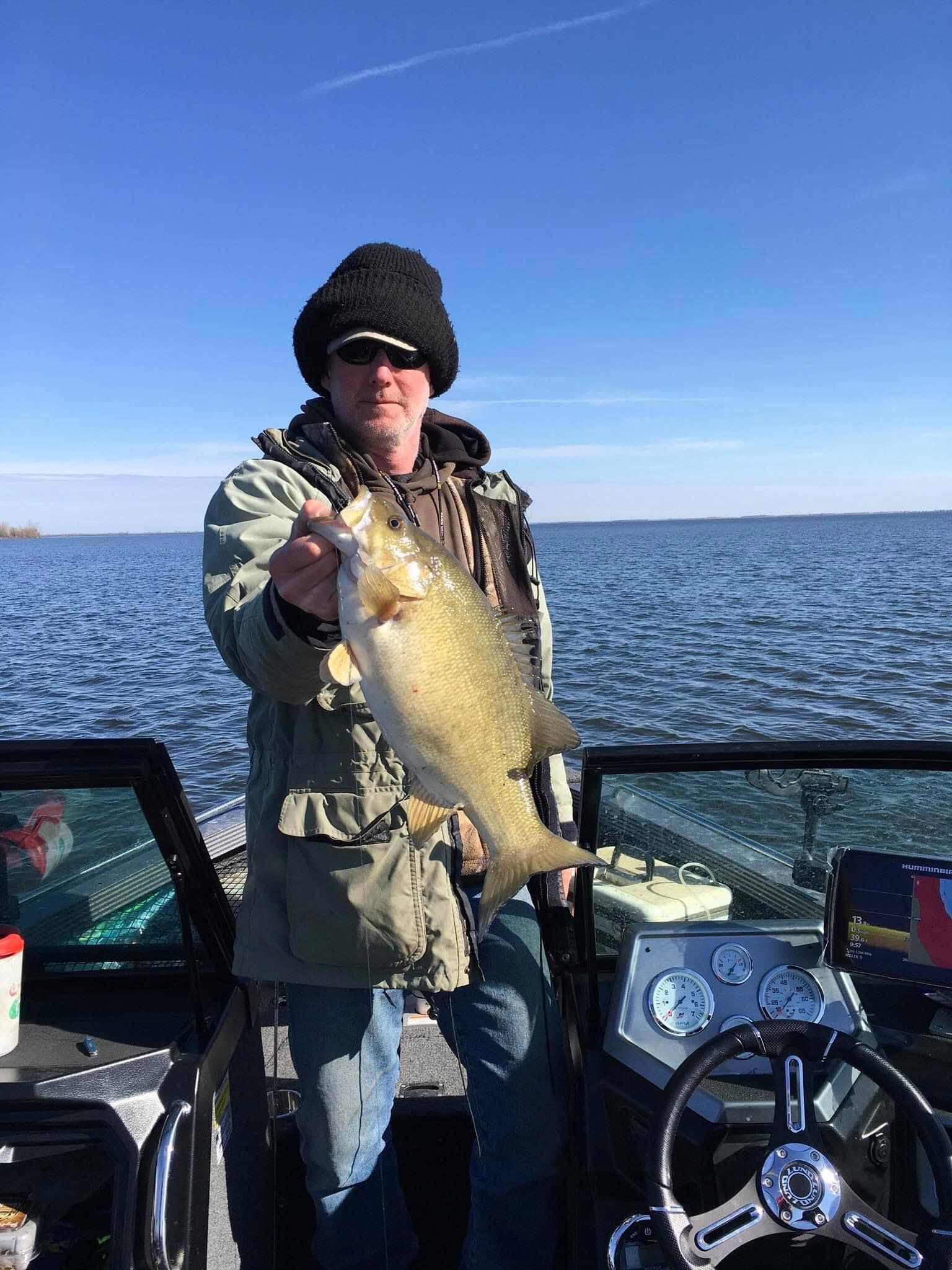 Man on boat holding fish, blue water, sunny day.
