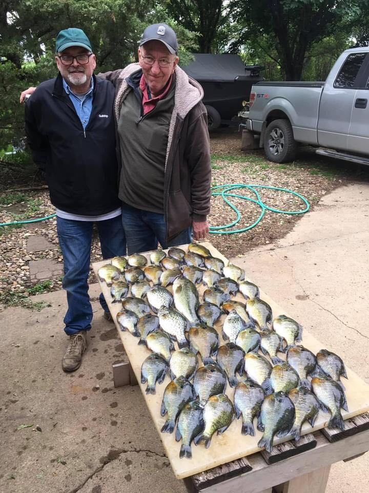 Two men pose with a table covered in freshly caught bluegill fish outdoors near a truck.