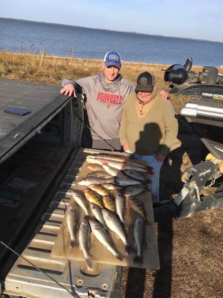 Two people stand near a truck bed filled with fish on a sunny day.
