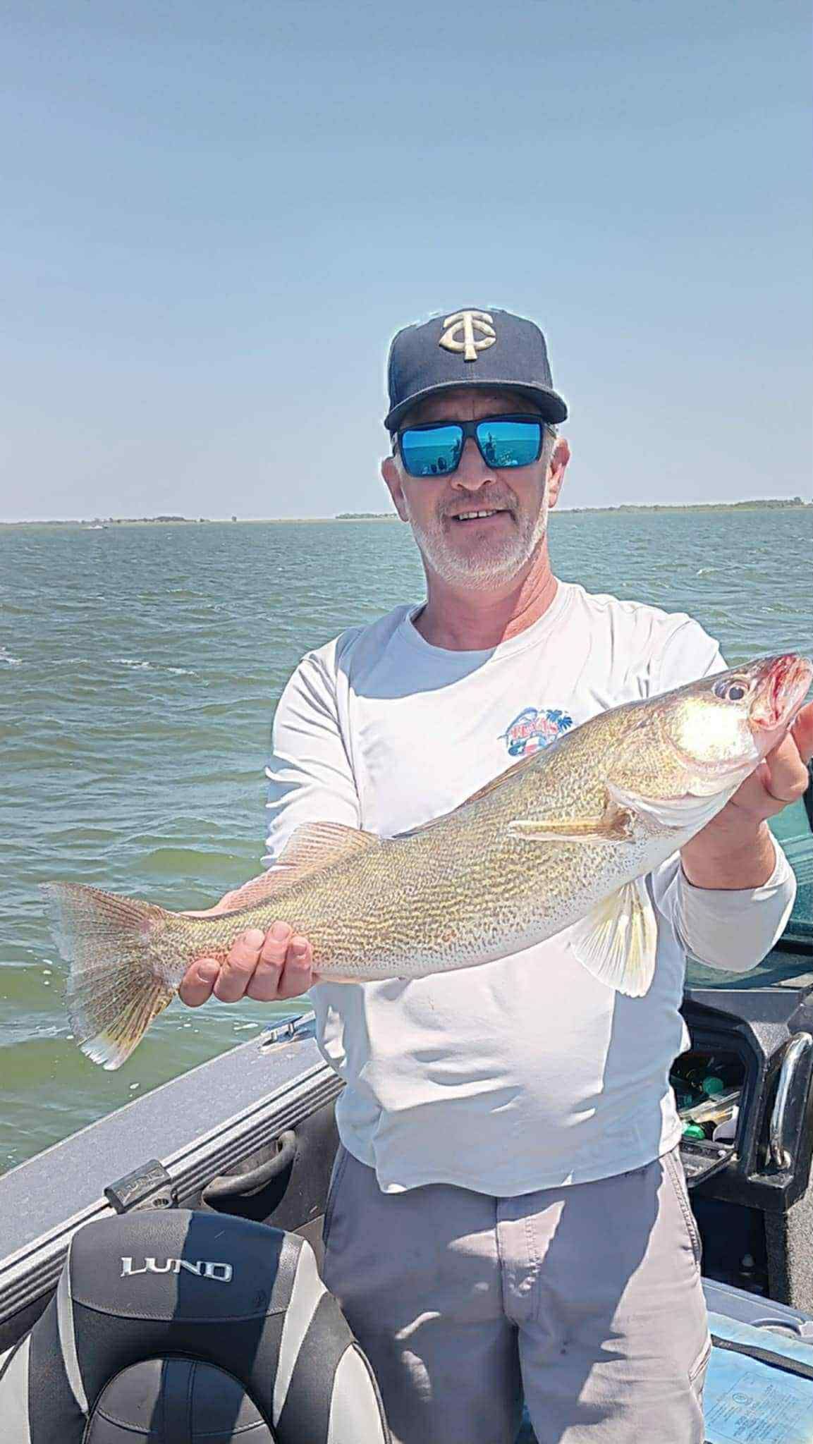 Man on a boat holding a large fish, sunny day, water in background.