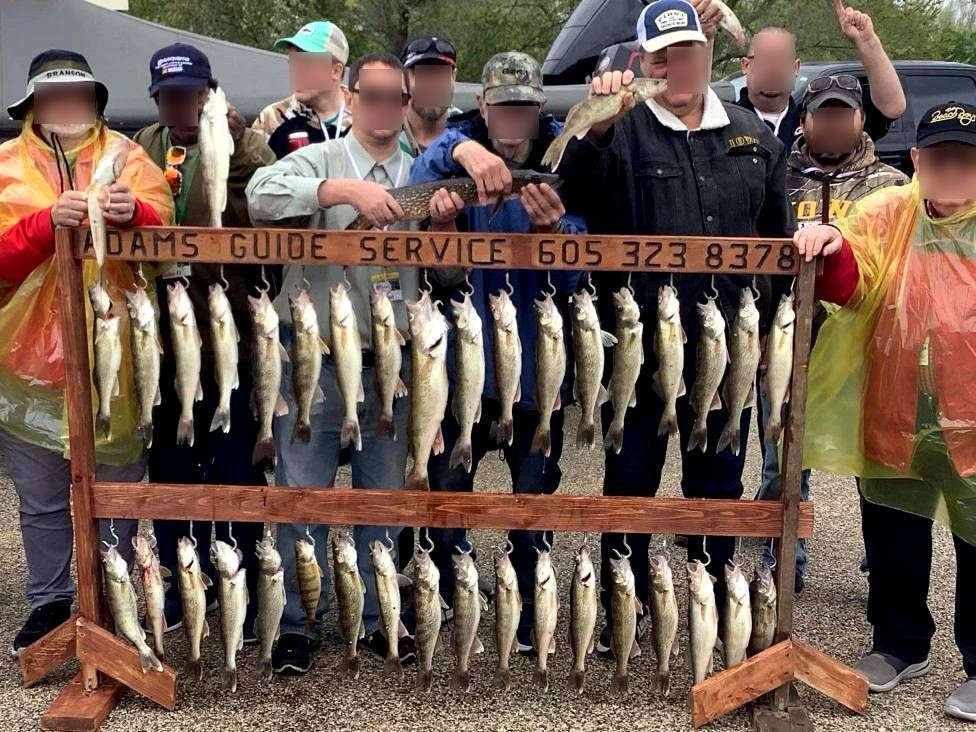 A group of people displaying many fish they caught on a rack; the sign says