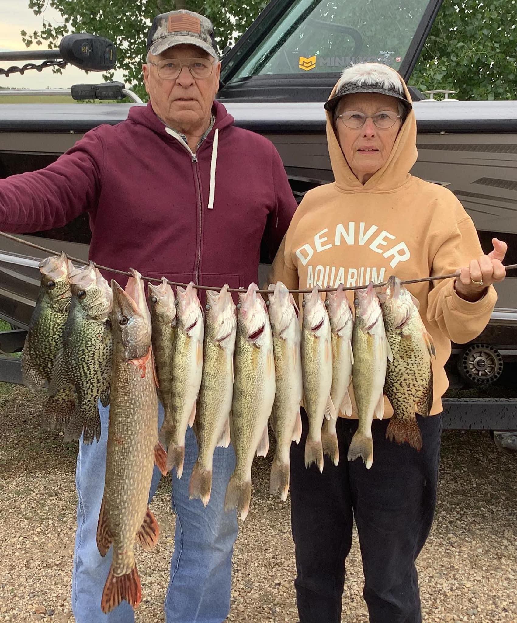Two people holding a string of fish they caught. One wears a hoodie and hat, the other a cap.