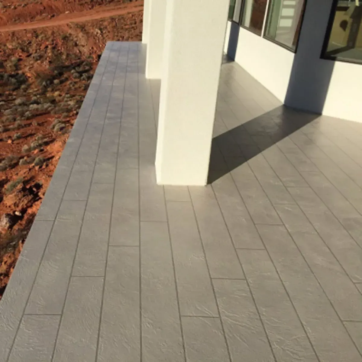 Gray tiled outdoor patio with white columns, overlooking a desert landscape.