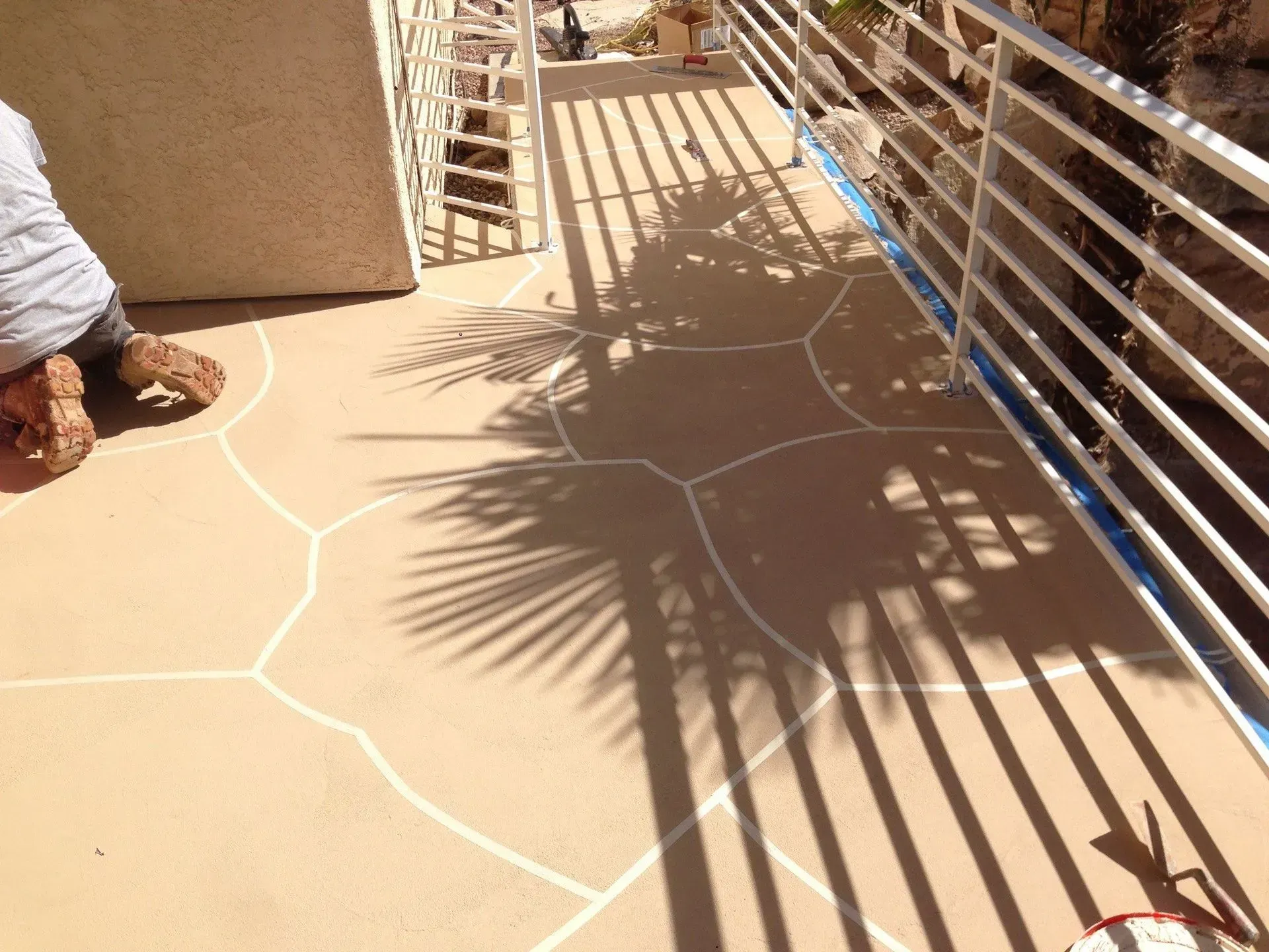 Person kneeling on a beige patio with white lines outlining sections. Sunlight casts a shadow.