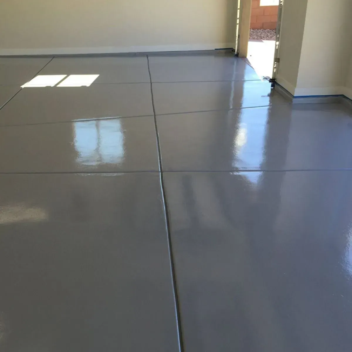 Shiny, gray epoxy-coated garage floor. Sunlight reflects in the surface, showing the room's empty state.