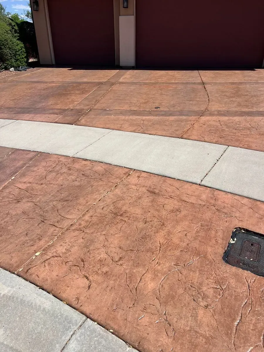 Brown stamped concrete driveway and sidewalk in front of a two-car garage with maroon doors.