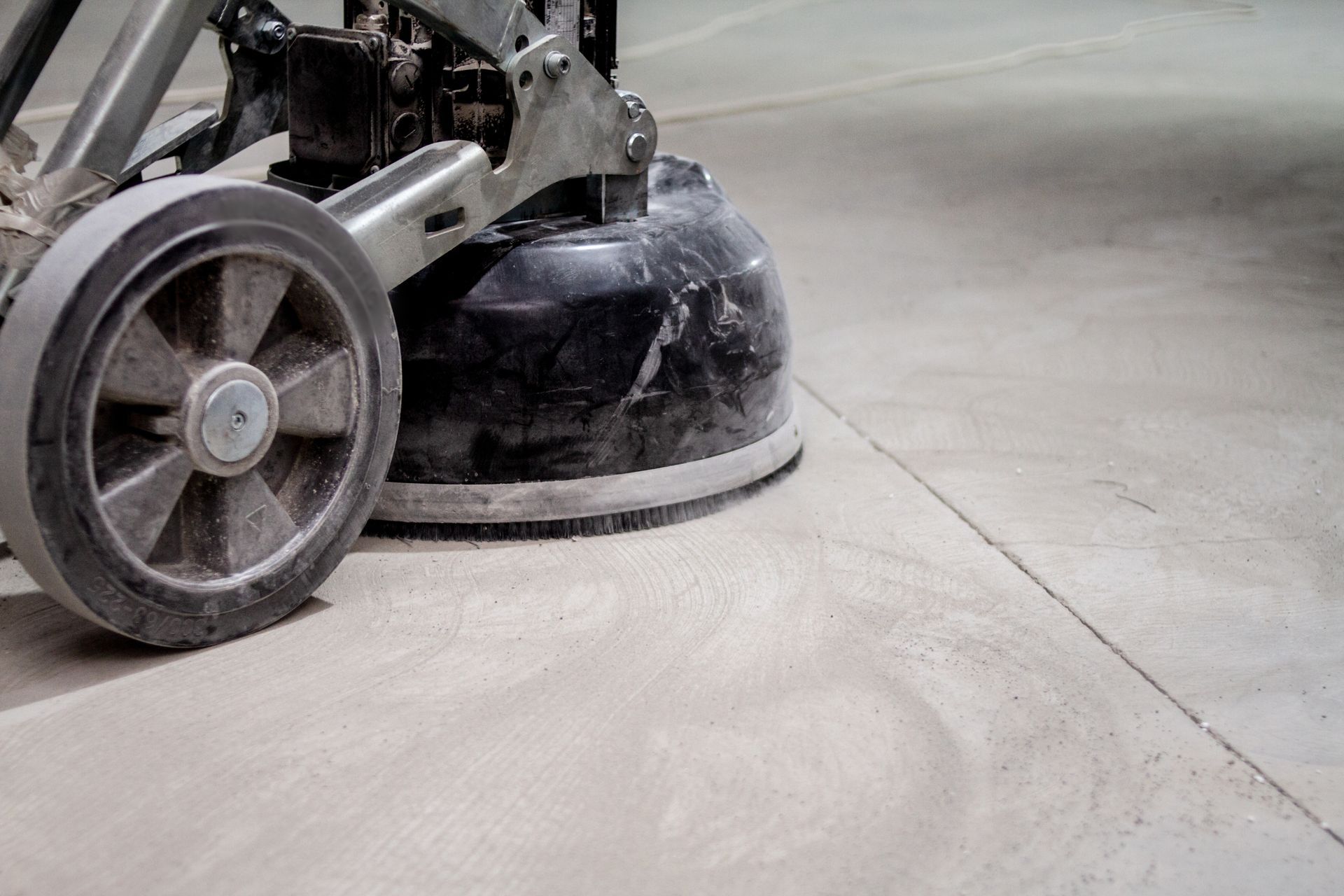 Concrete grinder in action, smoothing a floor surface with a wheel in view.