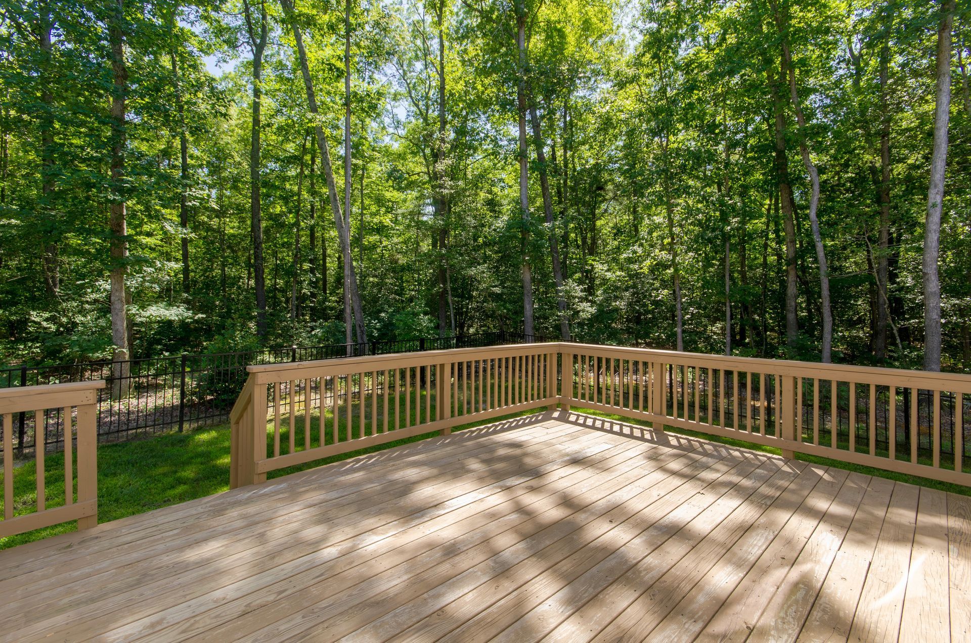 Wooden deck with a railing, overlooking a lush green forest.