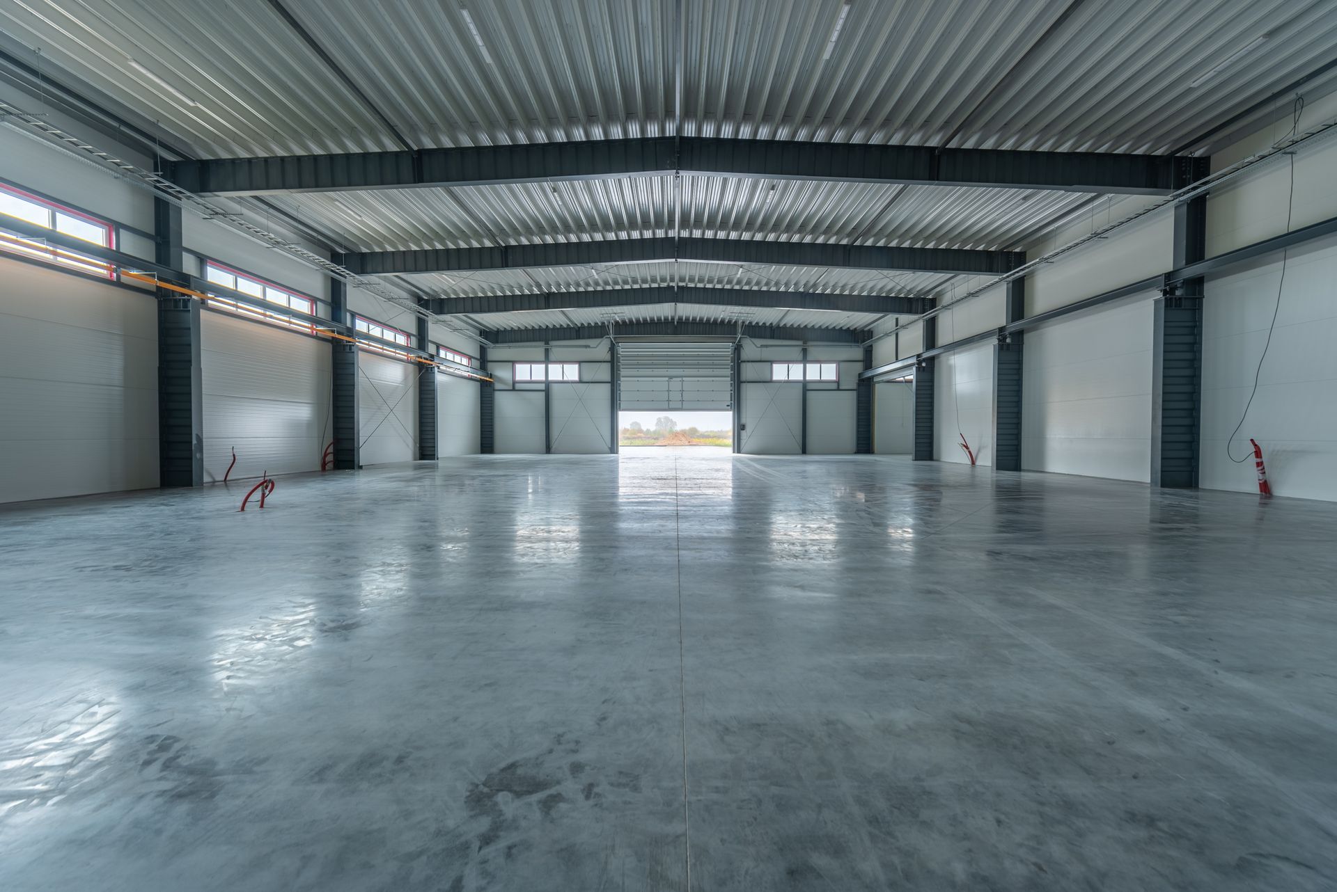 Inside of a spacious industrial warehouse with a concrete floor, metal beams, and white walls.