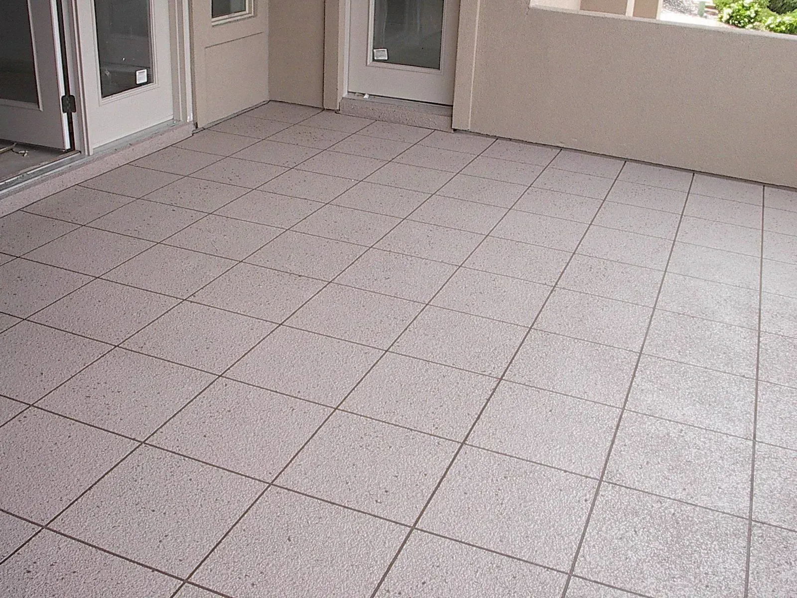 Tiled patio with light gray square tiles, bordered by white doors and a beige wall.