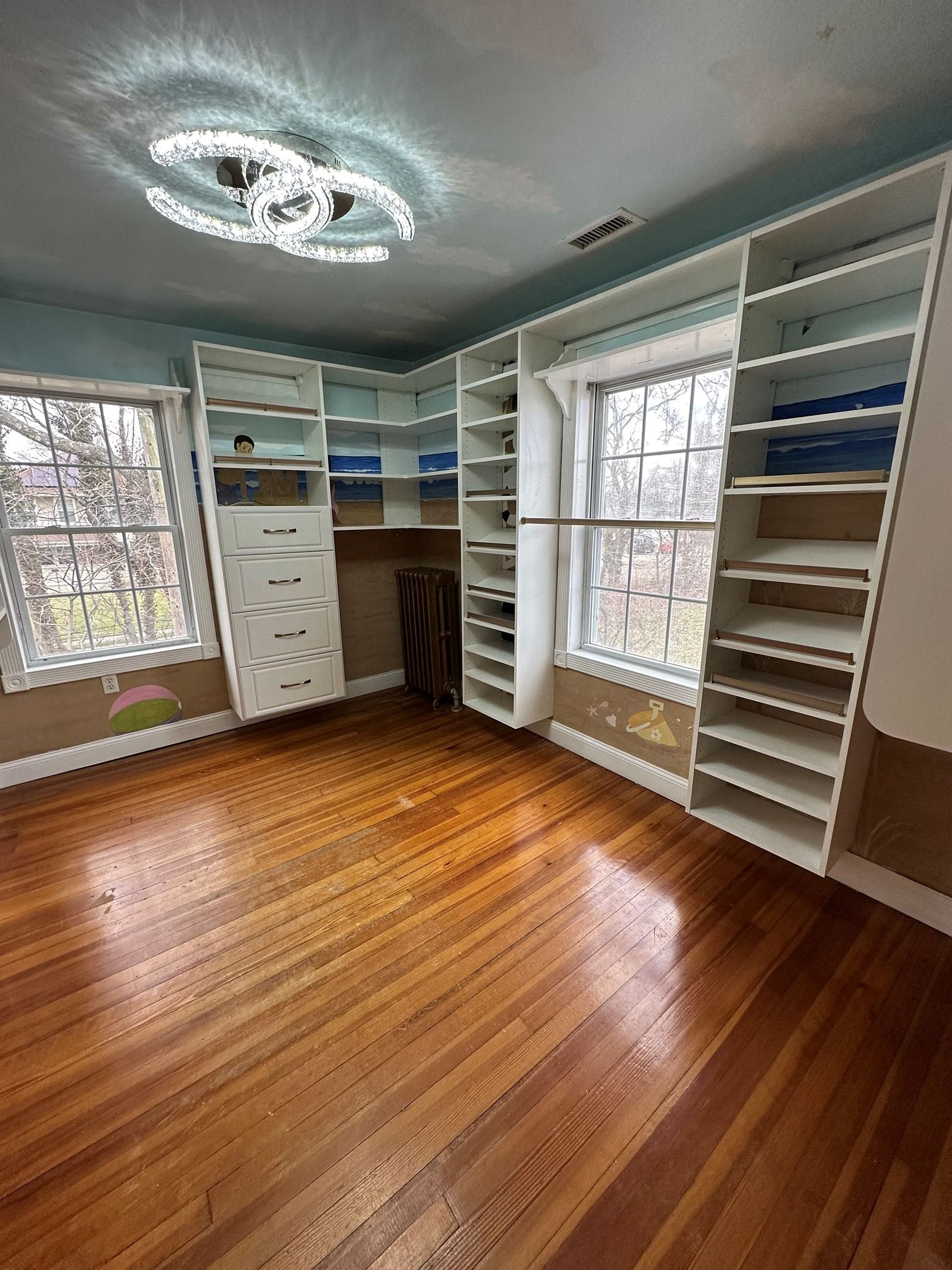 A large walk in closet with hardwood floors and lots of shelves.