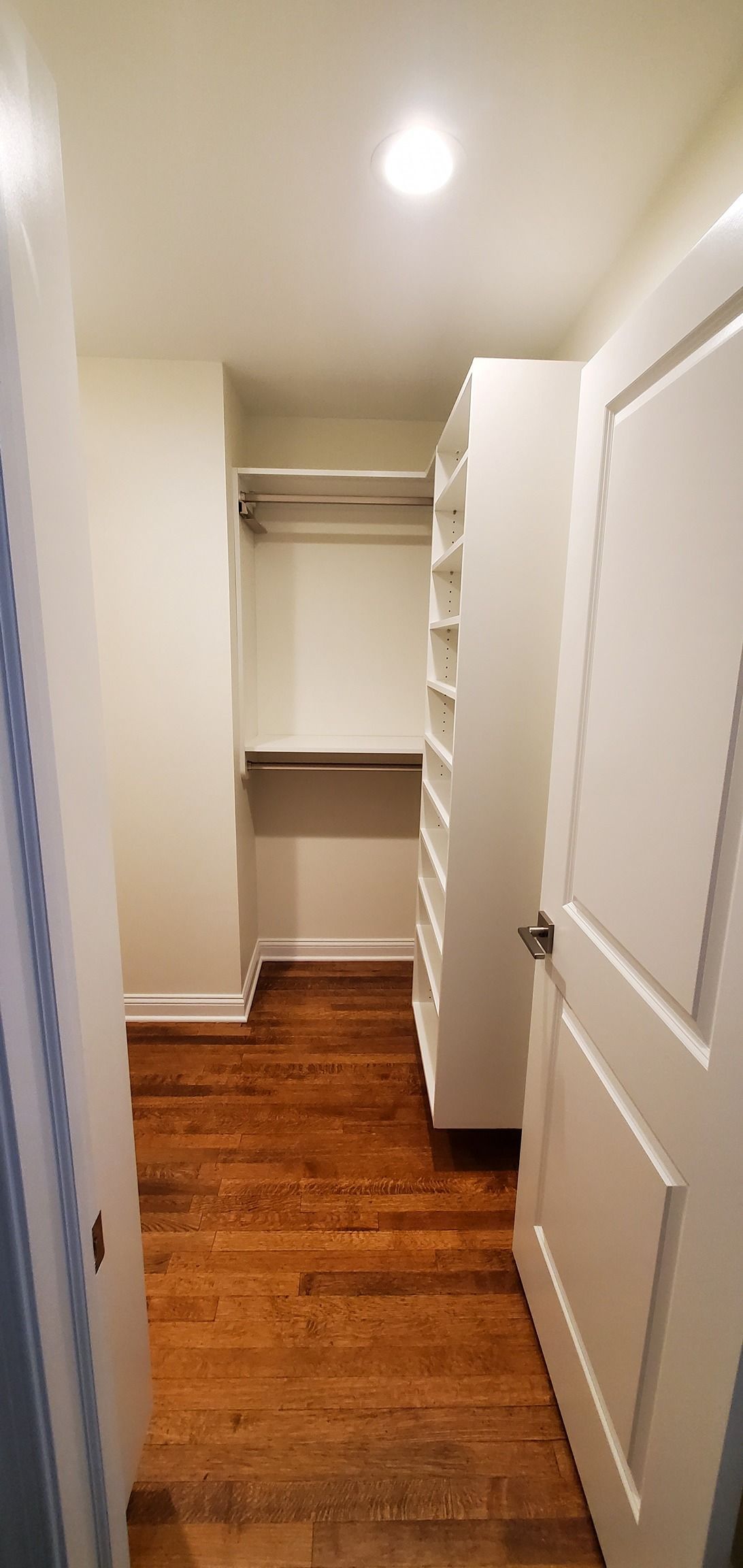 A walk in closet with hardwood floors and white shelves.