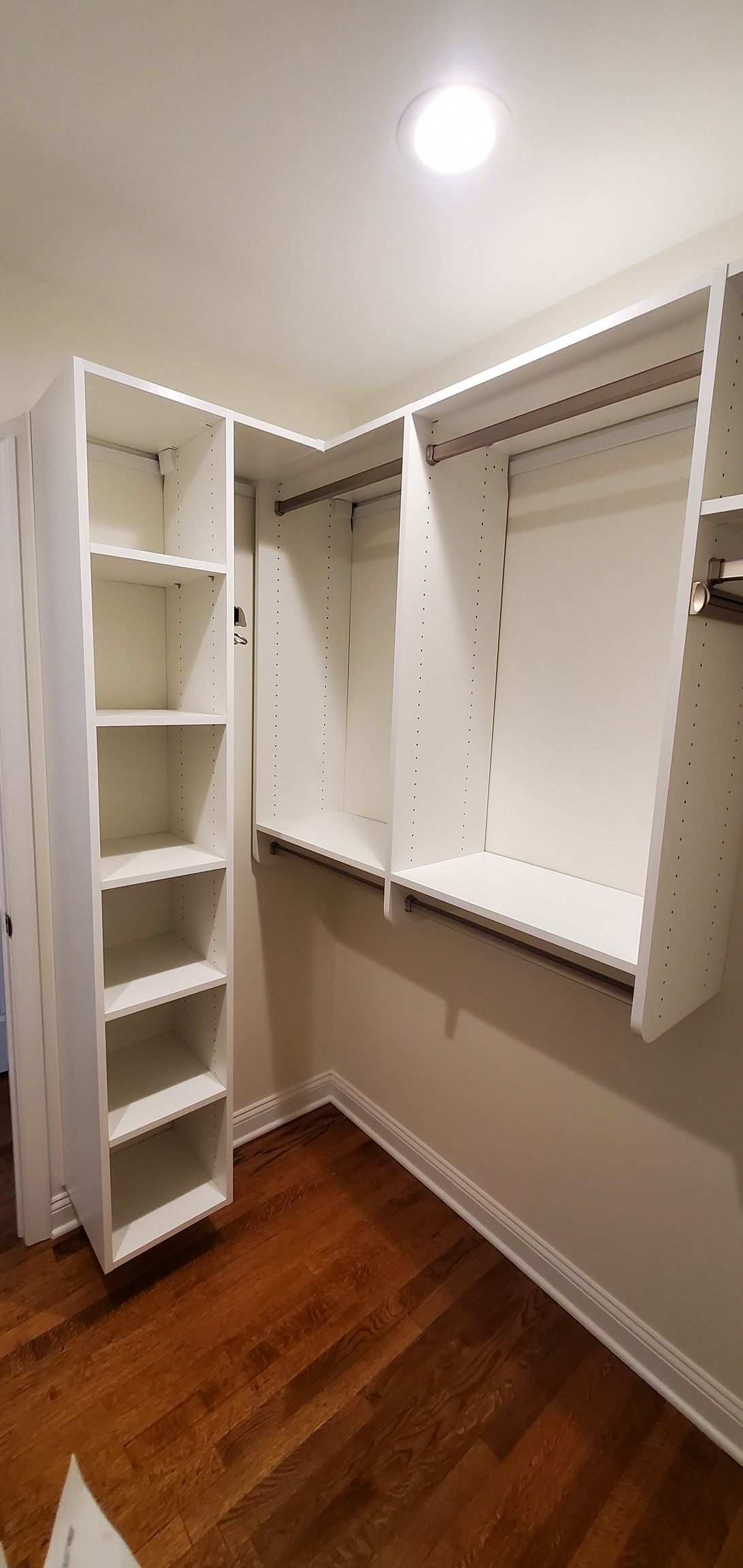 A walk in closet with wooden floors and white shelves.