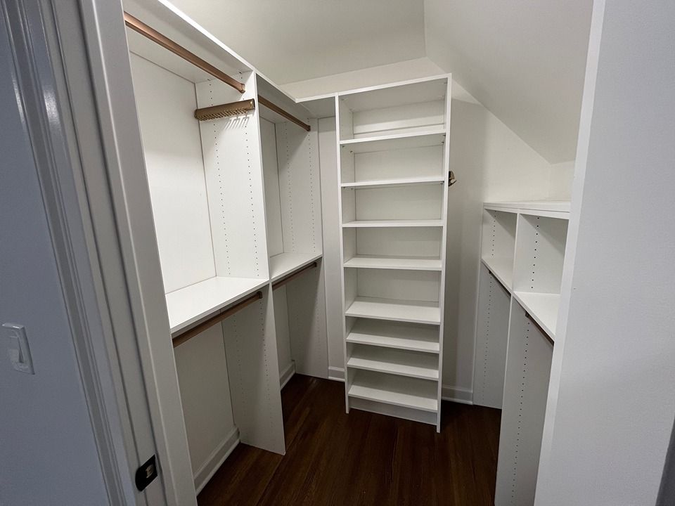 A walk in closet with white shelves and a wooden floor.