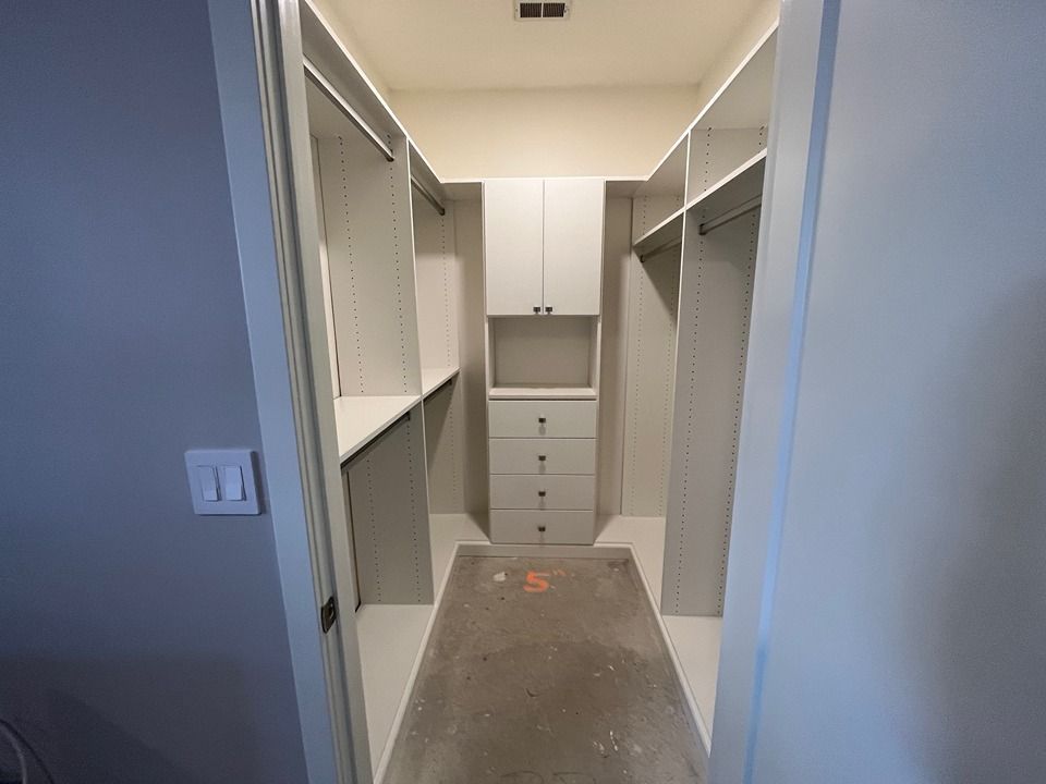 A walk in closet with white cabinets and drawers in a house.