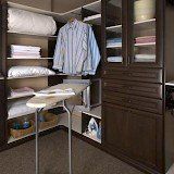 A walk in closet with a ironing board and a striped shirt hanging on the wall.