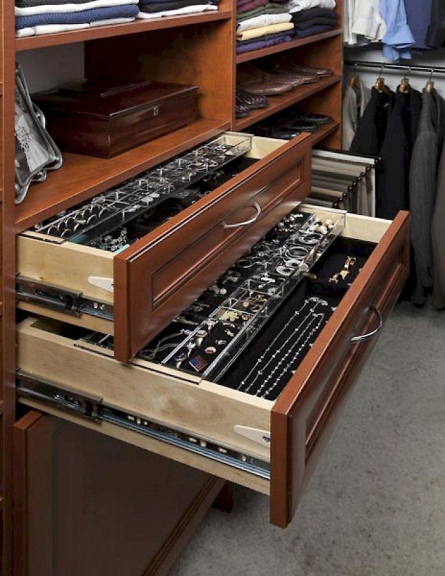 Wooden closet drawers filled with jewelry and ties, with clothing on shelves above and to the side.